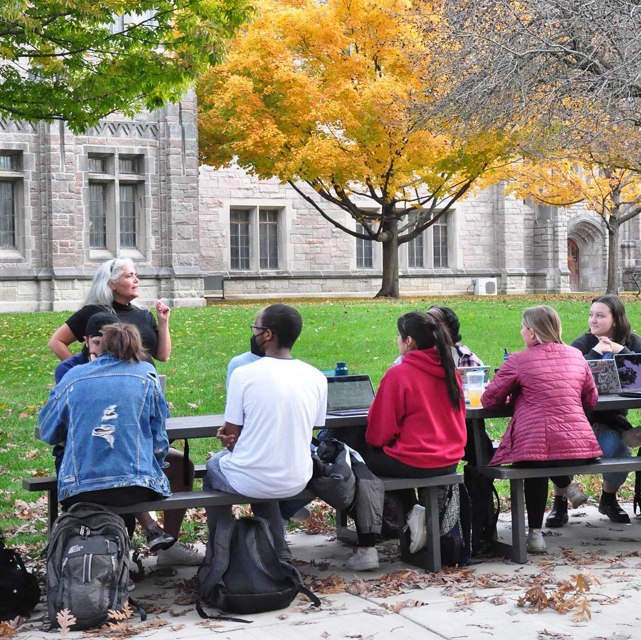 students outside on picnic table being taught by woman with grey hair
